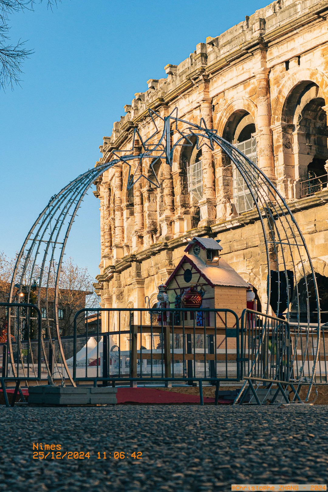 Les arènes de Nîmes décorées pour Noël, avec une arche lumineuse et un chalet festif.