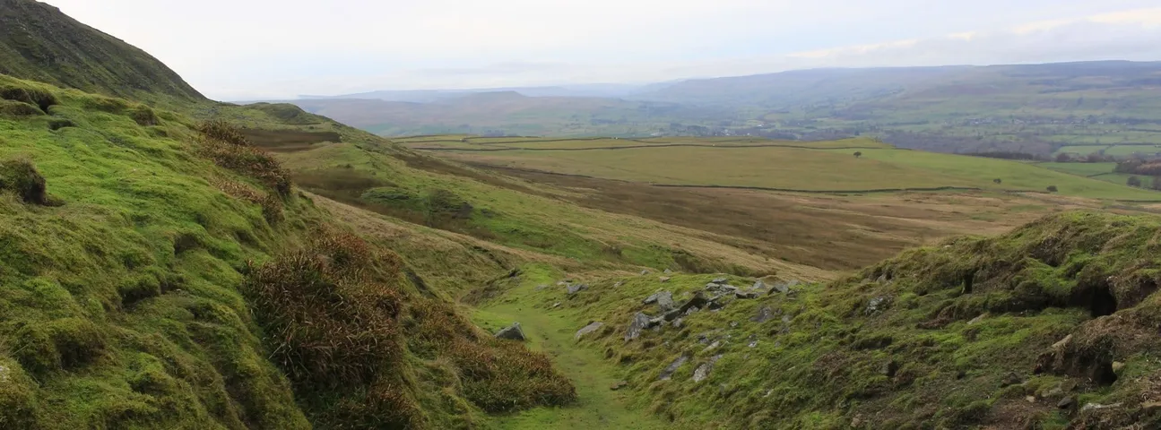 Sweeping panoramic view of rugged moorland hills with winding valley and vast open countryside stretching to distant horizon