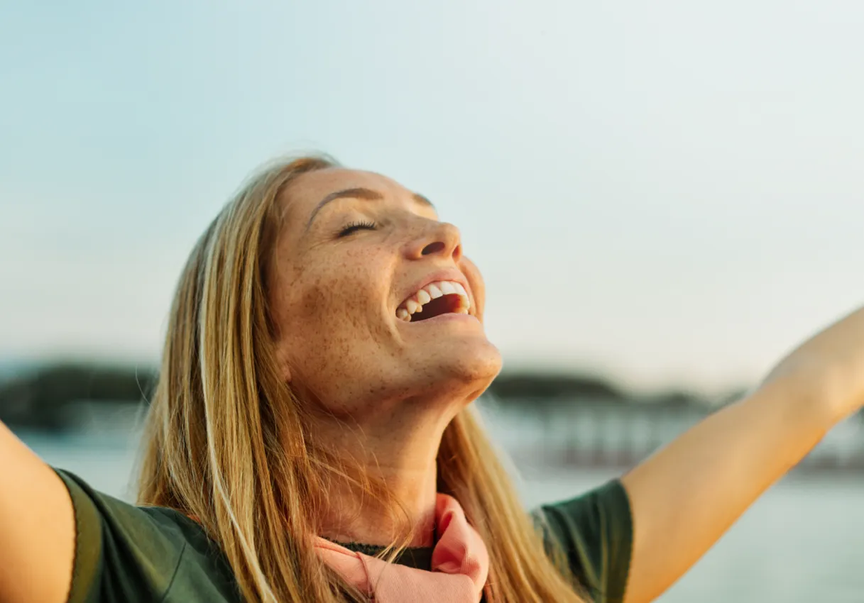 woman happy with freckles, arms up, eyes closed
