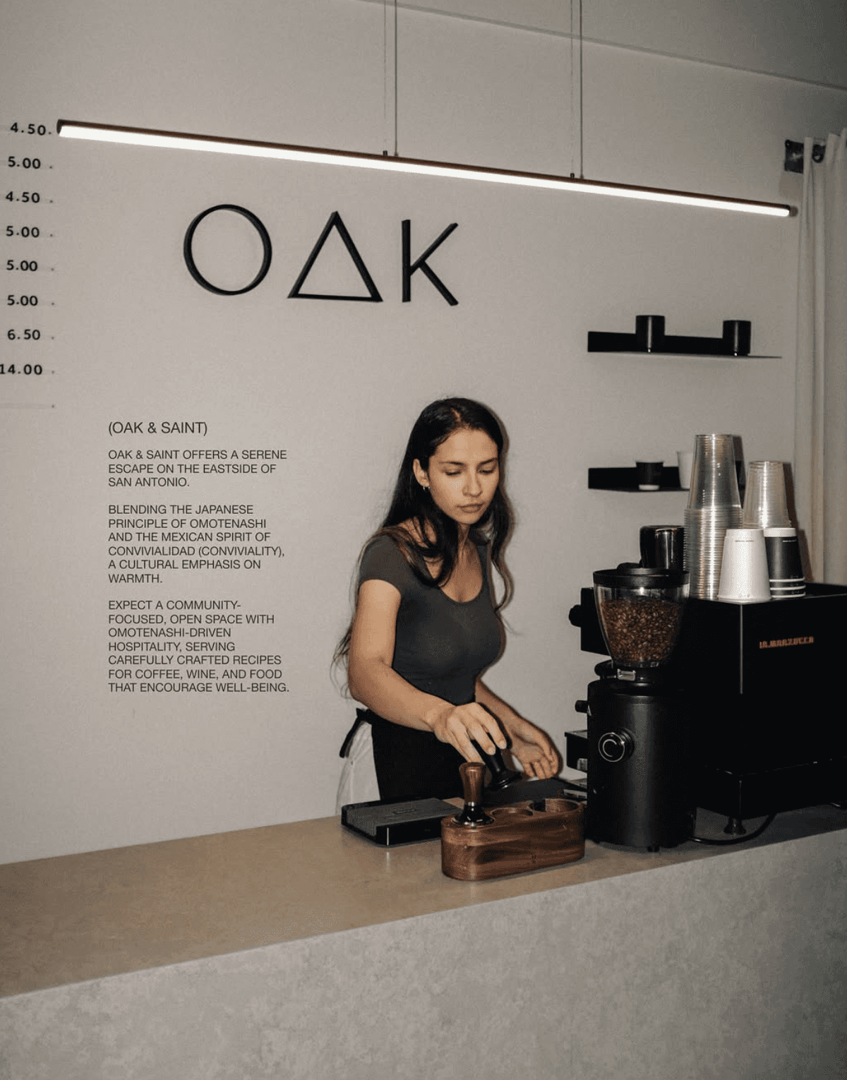 Barista preparing coffee beneath dimensional OAK wall logo inside Oak & Saint café and wine bar.