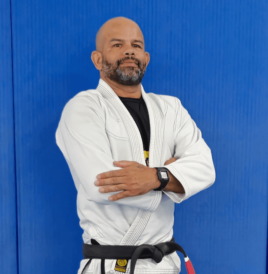 Tony “Ourico” in a white gi, arms crossed, standing confidently in front of a blue background