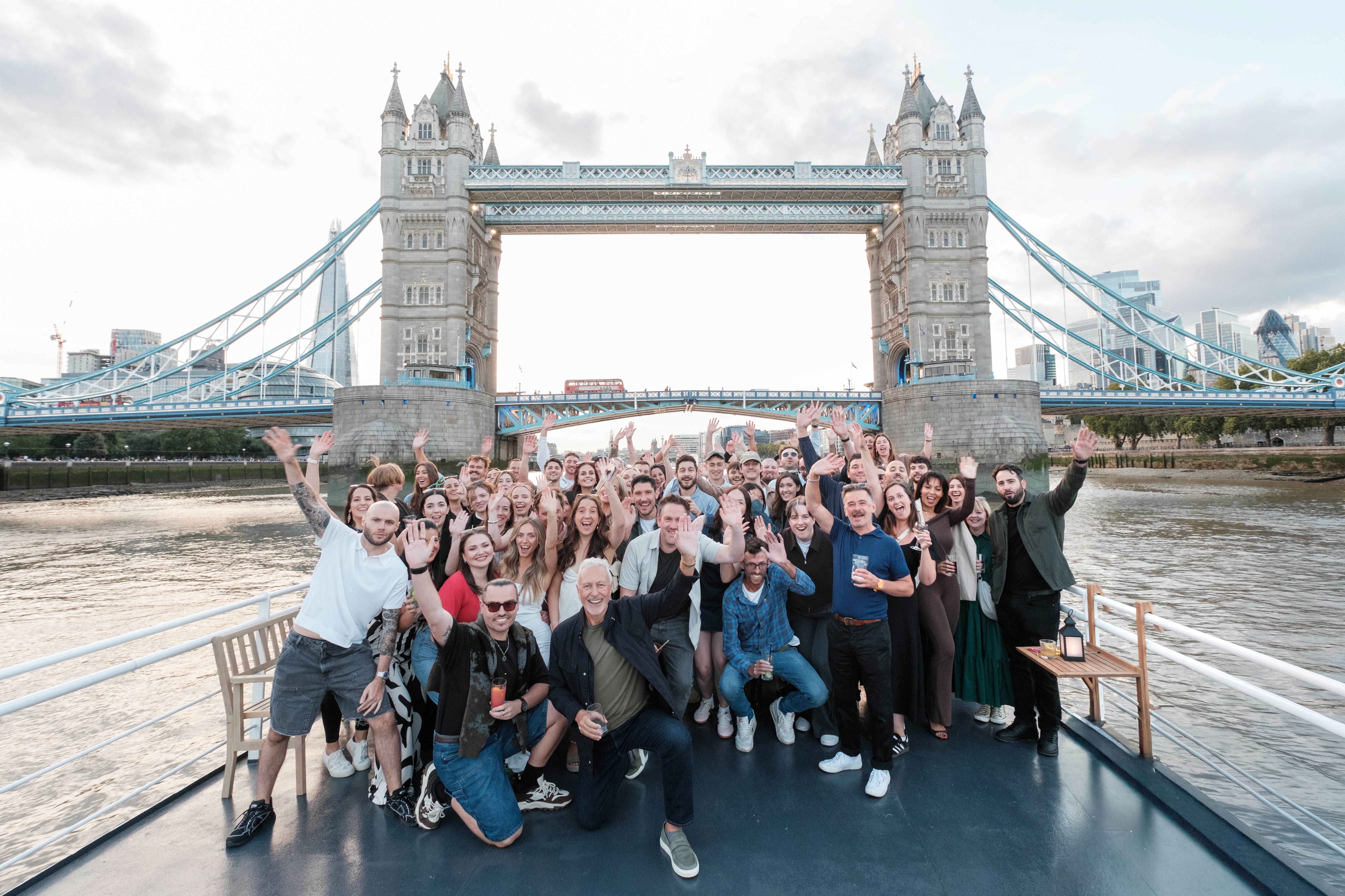 Group of people posing together on a bridge with the Tower Bridge visible in the background.