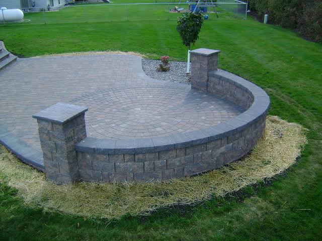 Installation of a paver patio and a semicircular stone retaining wall in a residential garden.