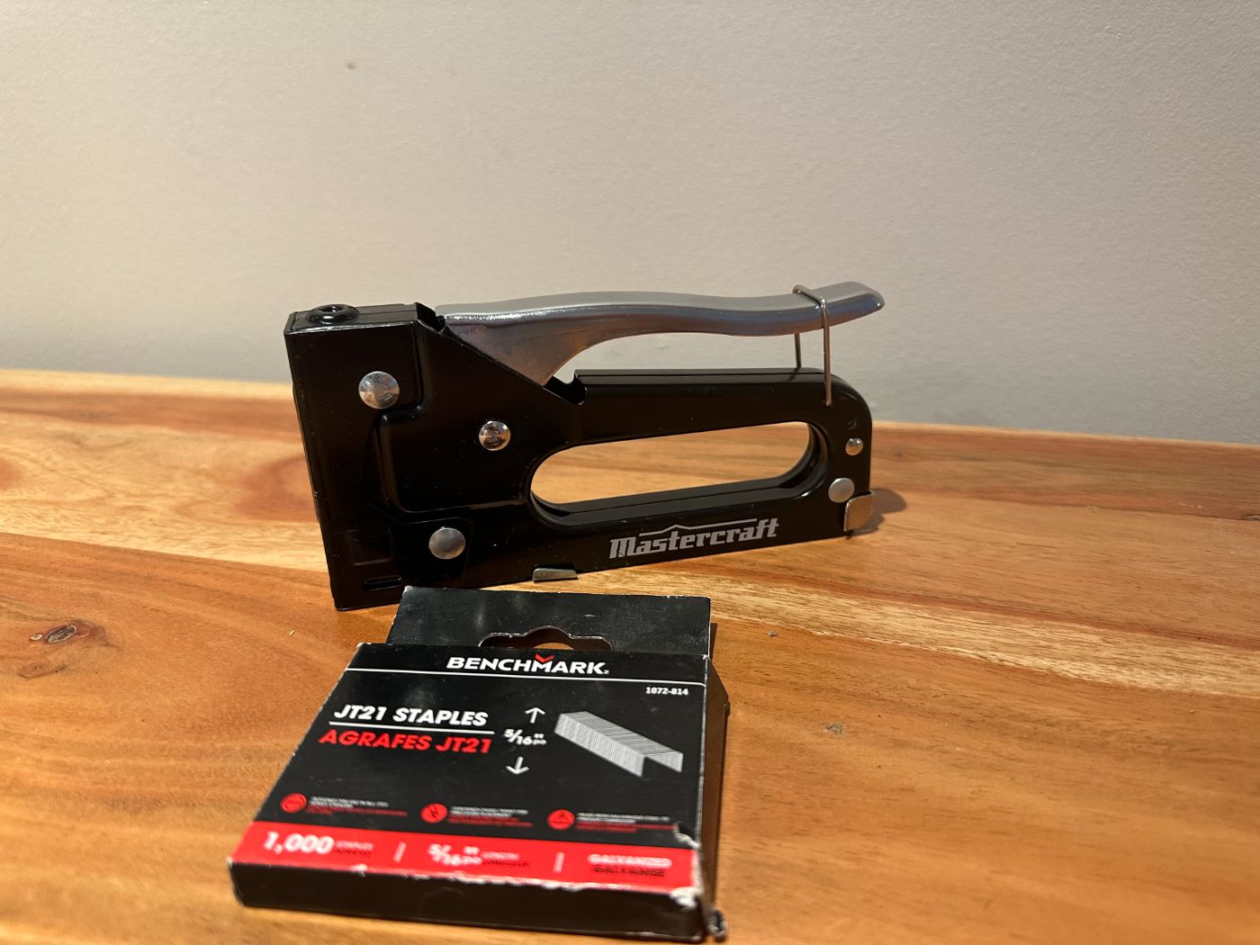 Agrafeuse manuelle Mastercraft noire avec boîte d’agrafes JT21 Benchmark, posée sur une table en bois