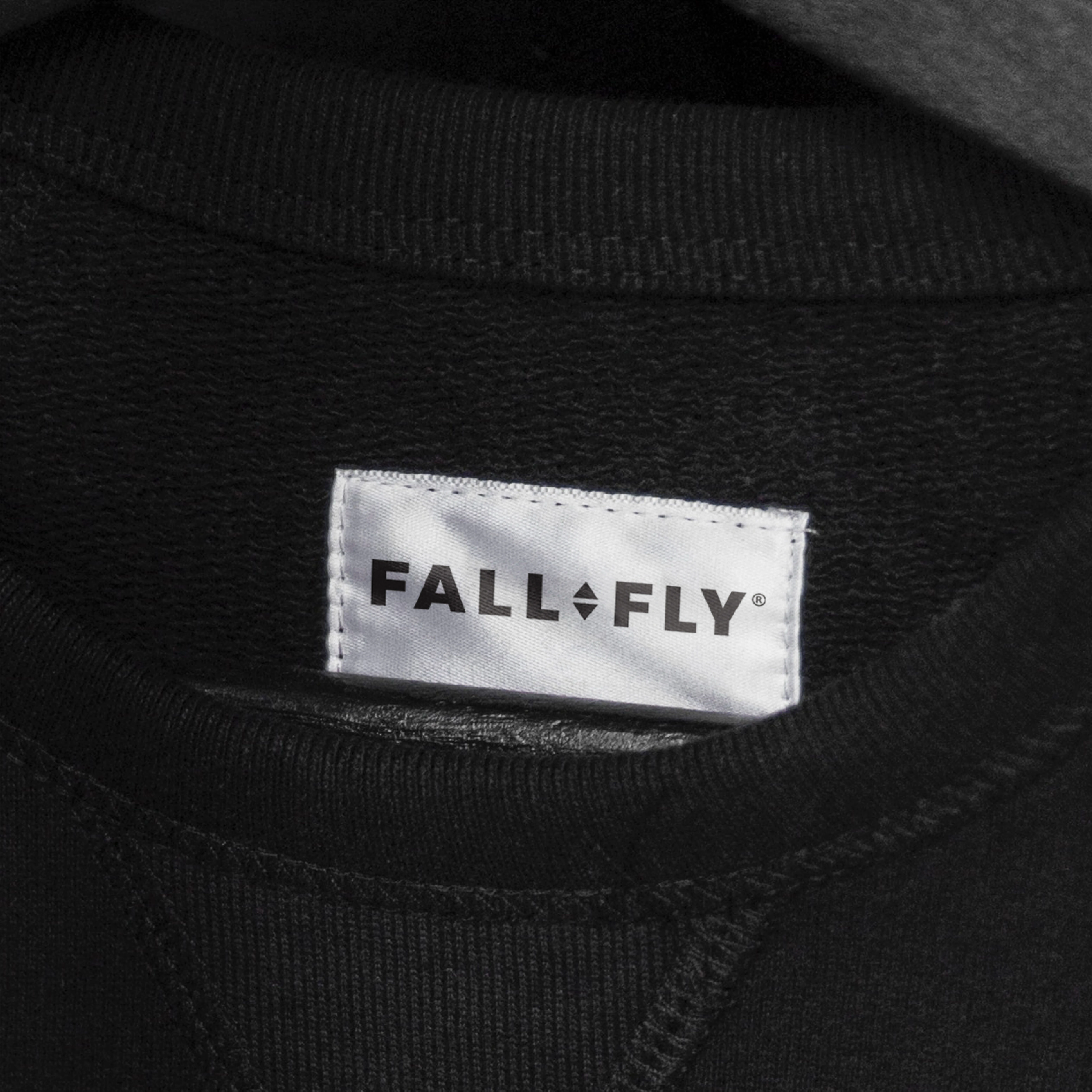 Fall fly- A white clothing label with the black text "FALL FLY" is sewn onto the neckline of a black garment.
