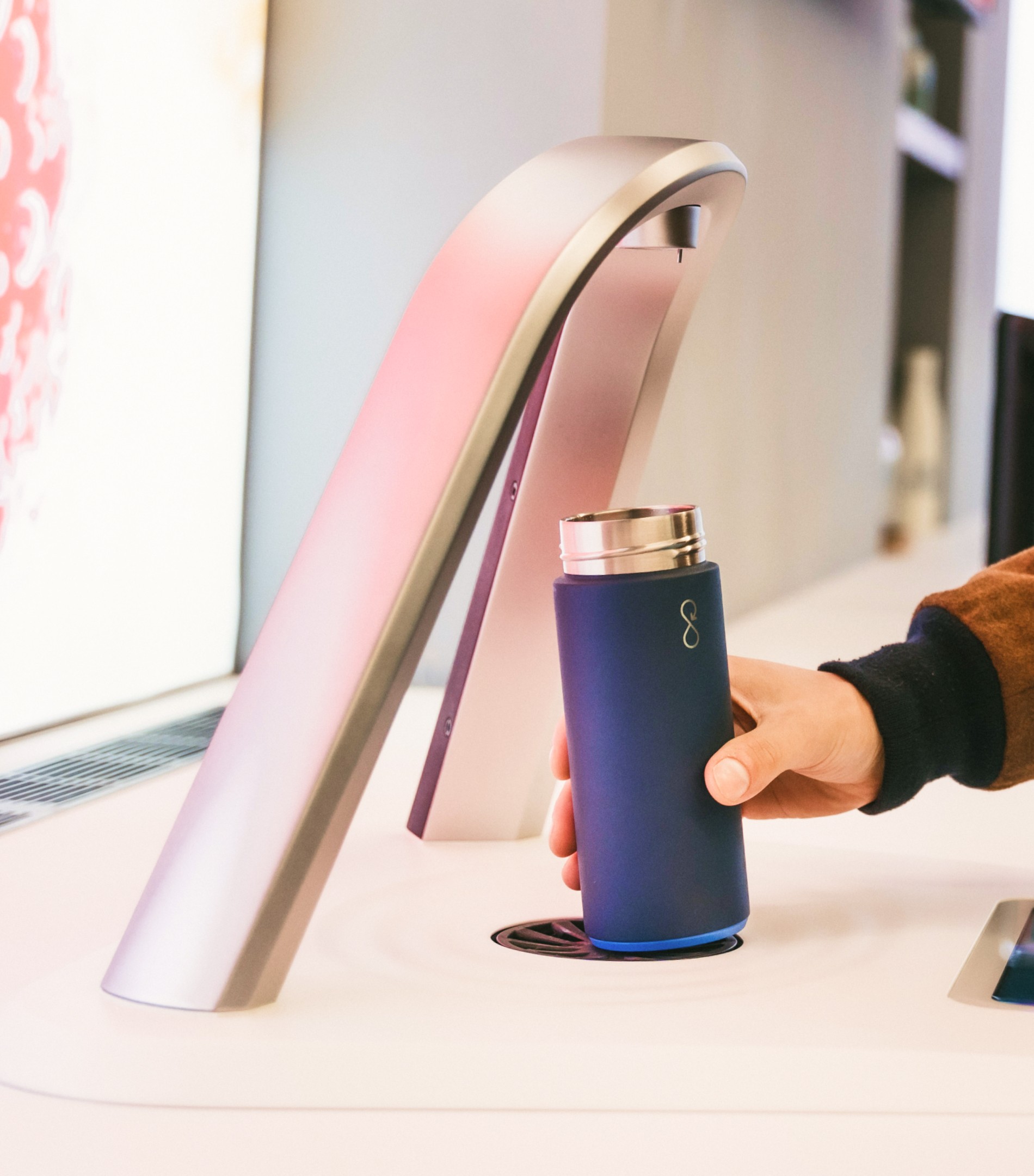 Hand placing a refillable bottle under the Aqua Libra smart dispenser in a retail environment