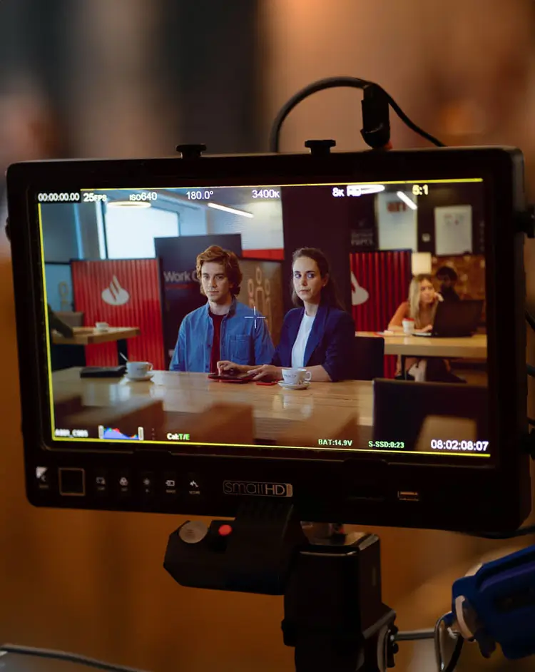 Portfolio Thankium: Personas sentadas en una cafetería filmadas en pantalla de cámara, fondo de trabajo y ambiente informal.