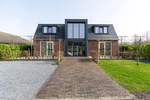 Een recht vooraanzicht van de vakantiewoning met een bestrate oprit en een glazen entree.