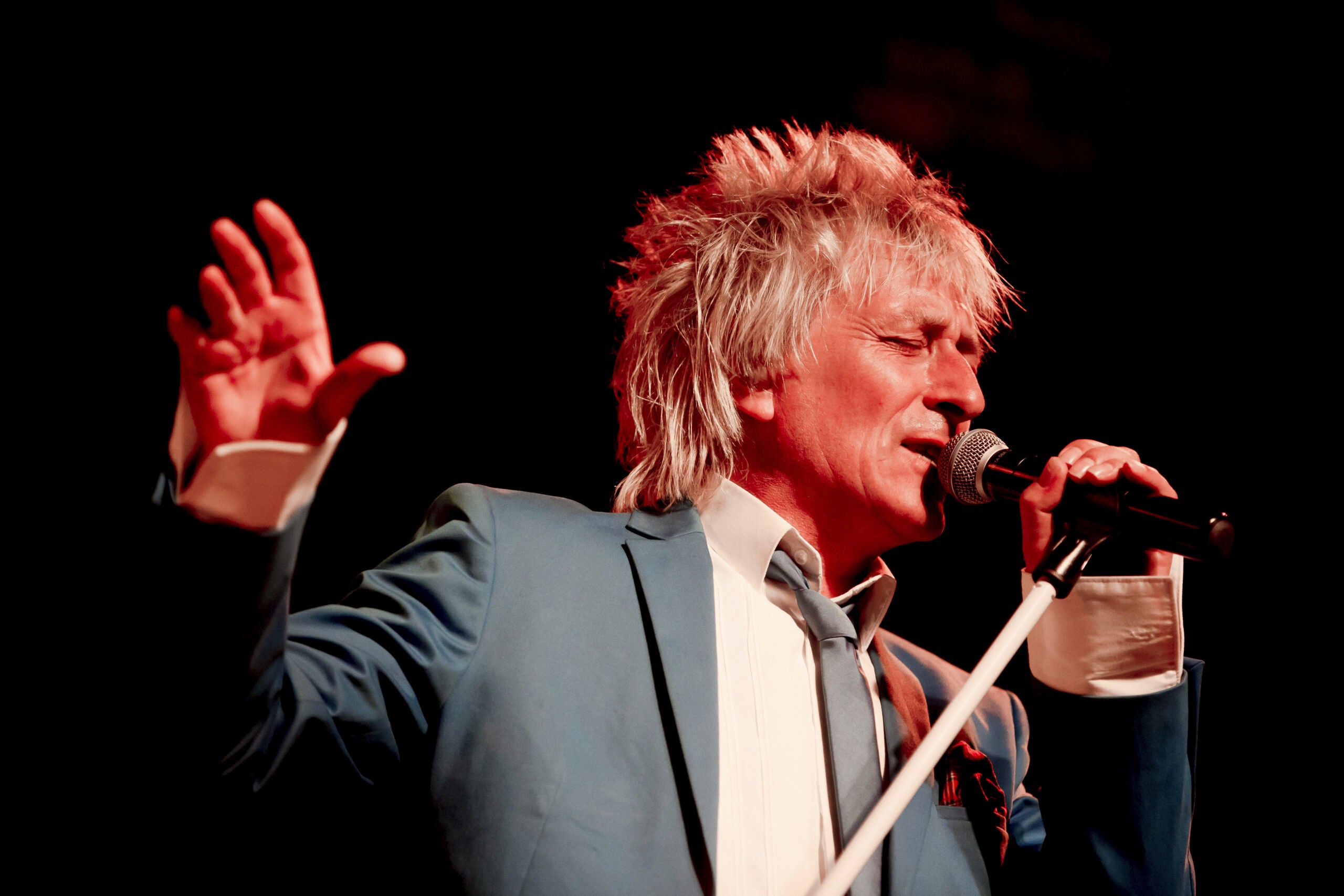 A rod stewart impersonator singing in a green jacket and tie