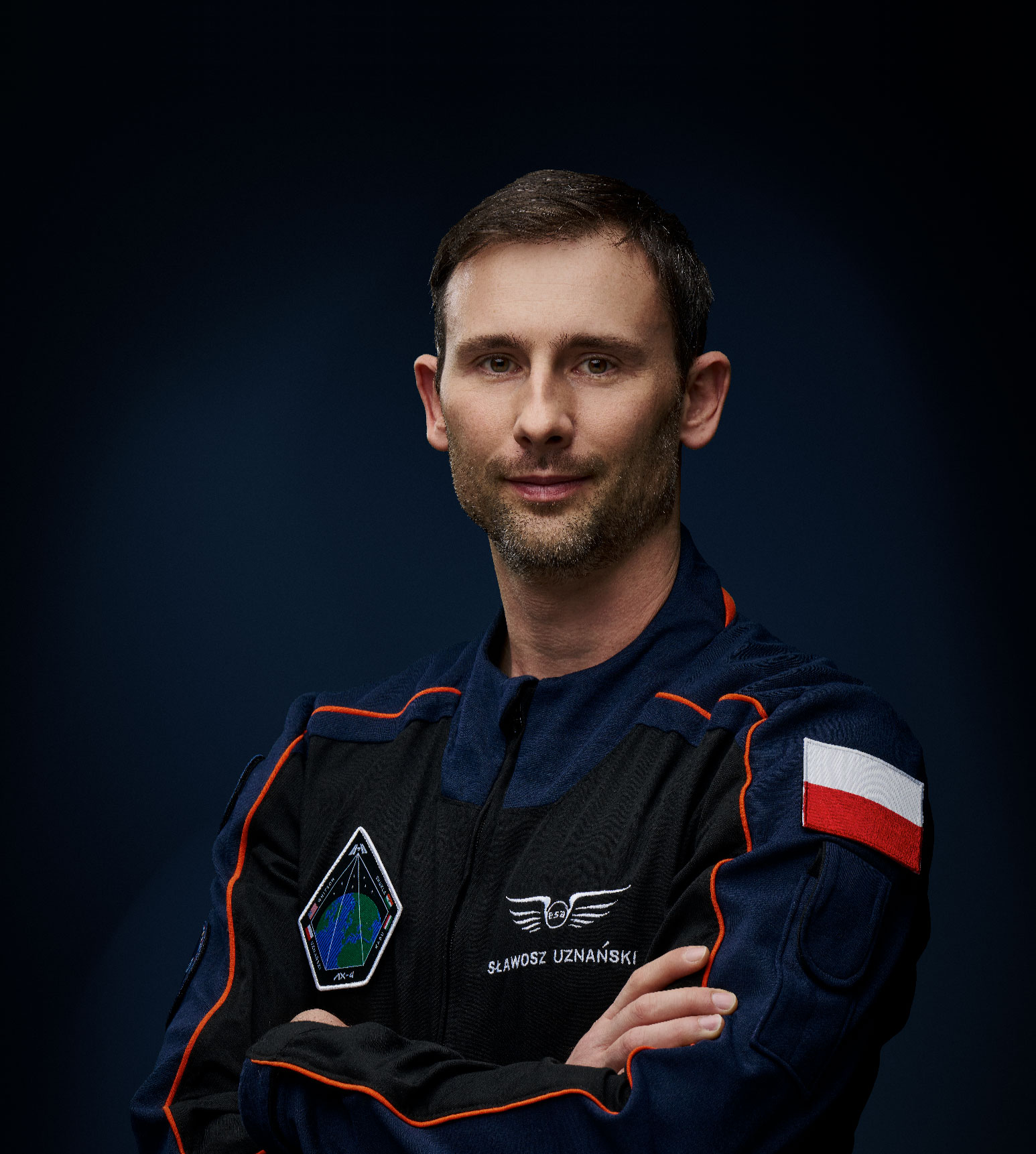 Sławosz Uznański - WIśniewski w oficjalnym kombinezonie astronauty z flagą Polski i logo ESA