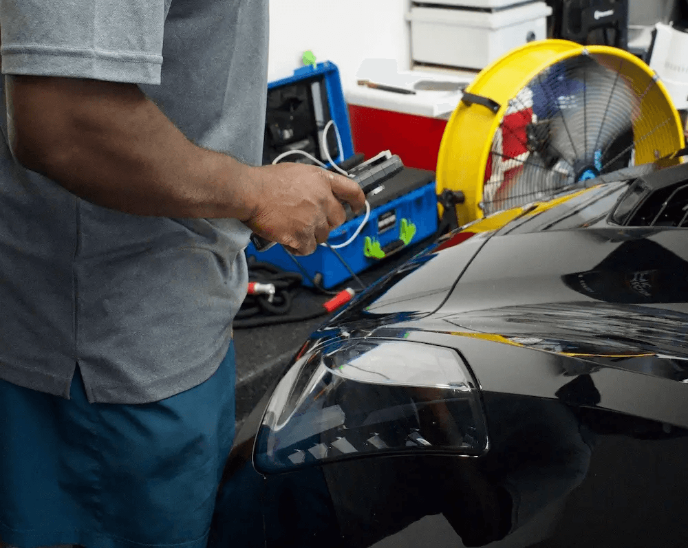 An auto detailer performing expert paint correction and scratch removal with a machine polisher on a black car hood for Tony Mobile Detailing in Leominster.
