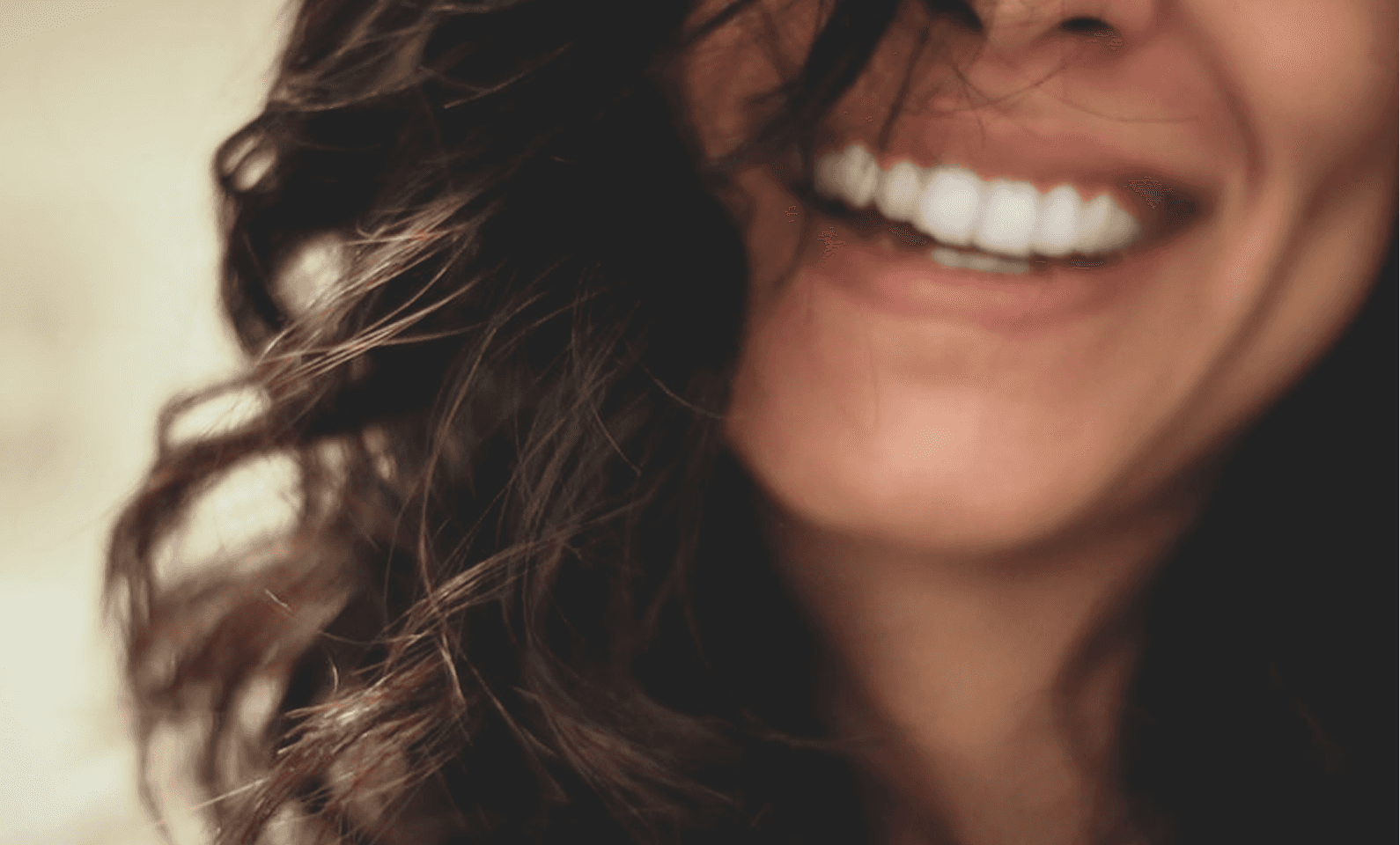 A smiling individual with wavy dark hair partially covers their face, showing white, bright teeth, evoking a sense of warmth and happiness.