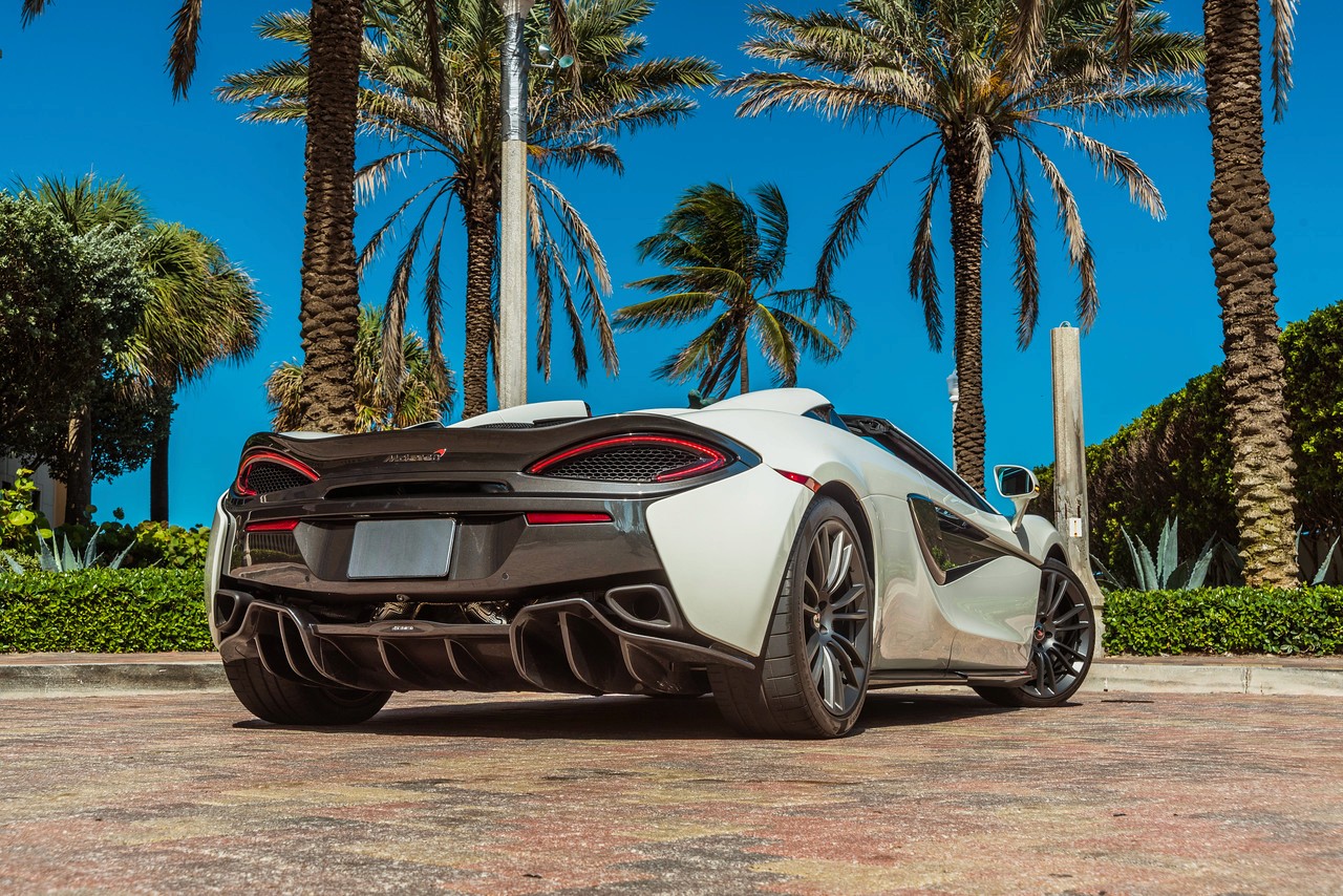 Side-rear perspective of the McLaren 570S, displaying its aerodynamic curves, large rear air intakes, and twin exhaust pipes.