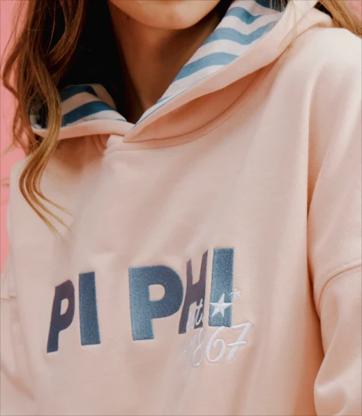 Close-up of a pale pink Pi Beta Phi hoodie with striped hood lining and embroidered lettering.