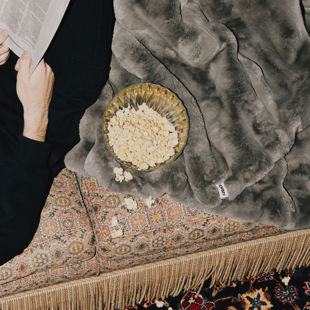 Blanket draped on couch with bowl of popcorn and man reading newspaper