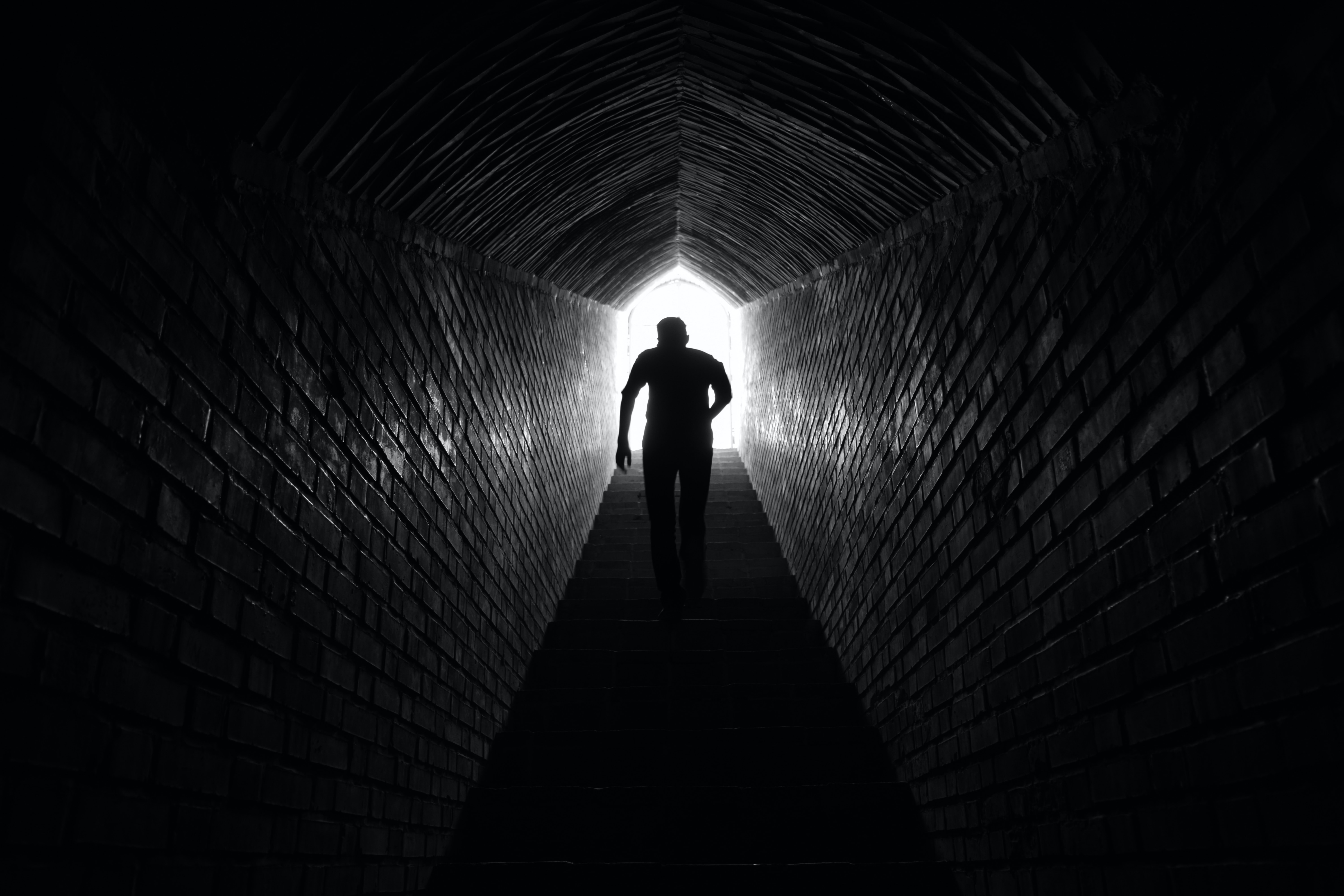 A man running down a walled alley with light behind him, very high contrast.