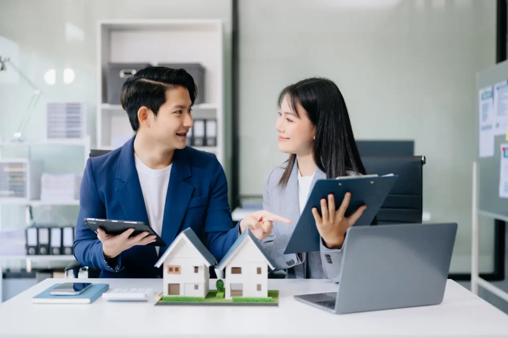 Rental property management software illustrated by a couple discussing real estate with house models and laptops.