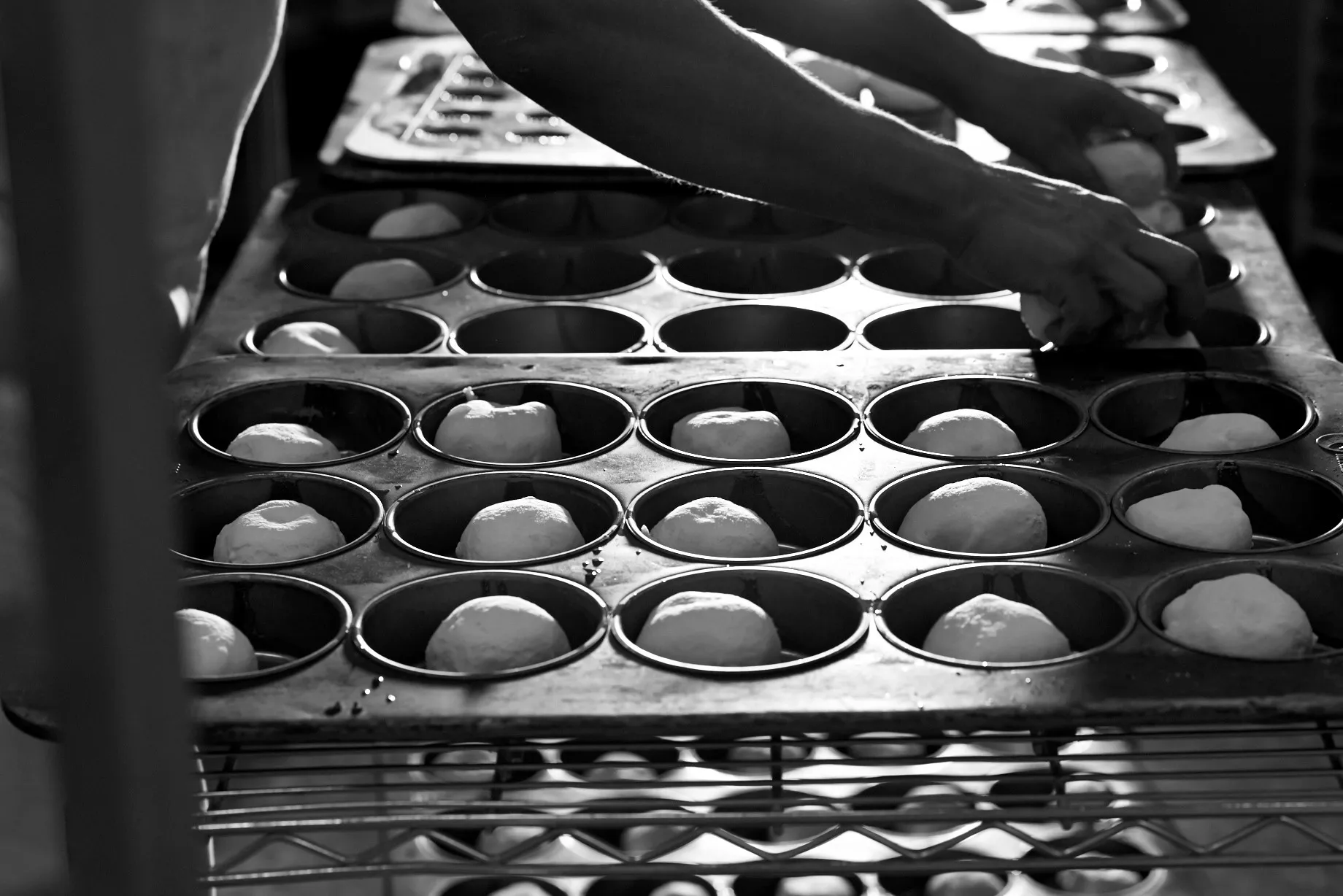 Fresh dough being hand crafted into baking trays before going in the oven