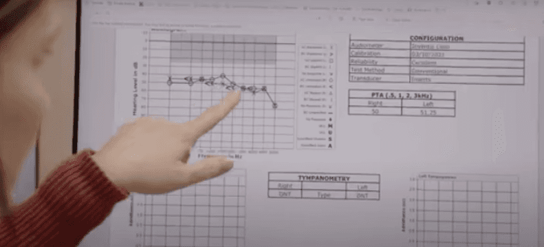 A woman with short hair looks thoughtfully at the camera, seated in a bright, modern room.