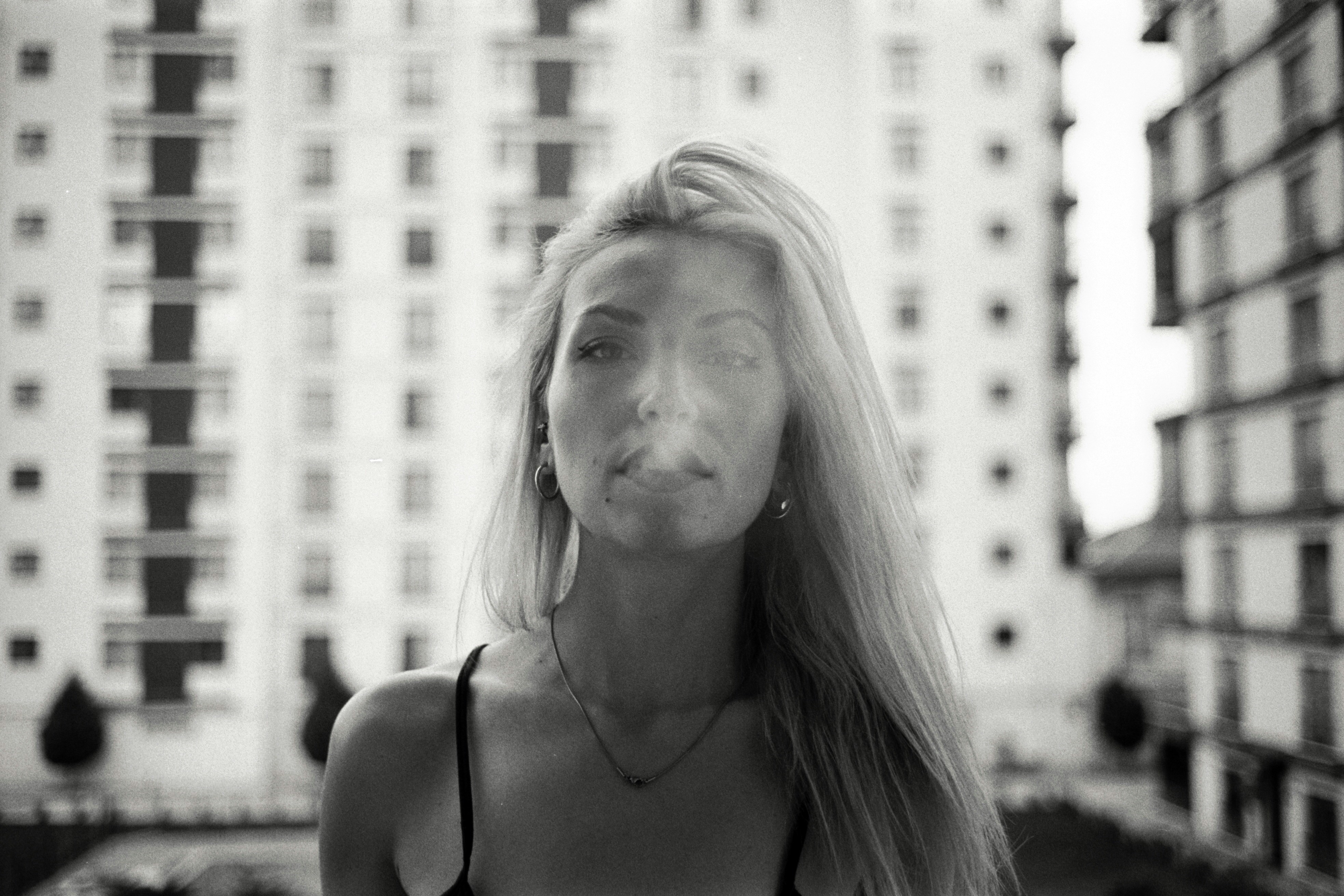 a woman blowing a cigarette in front of a tall building