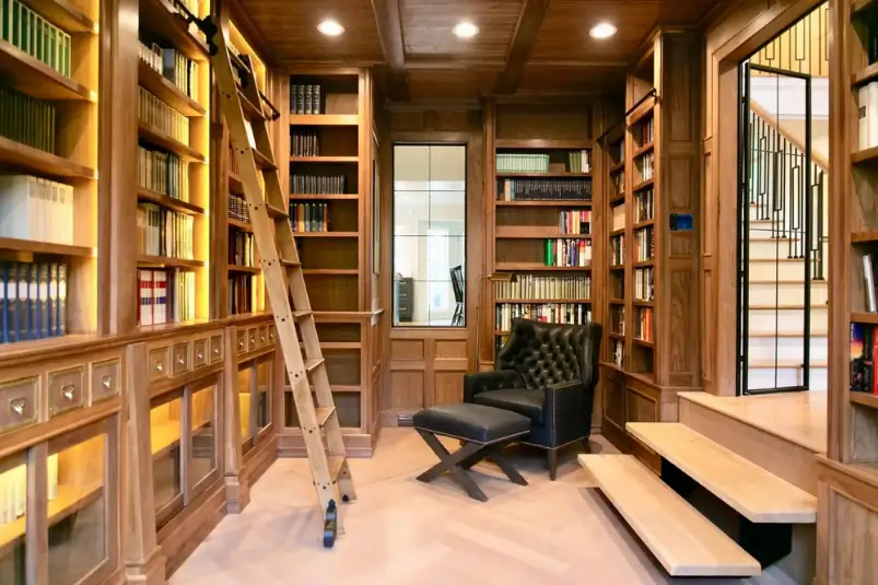 Custom wood home library with floor-to-ceiling bookshelves, rolling ladder, and black leather seating.