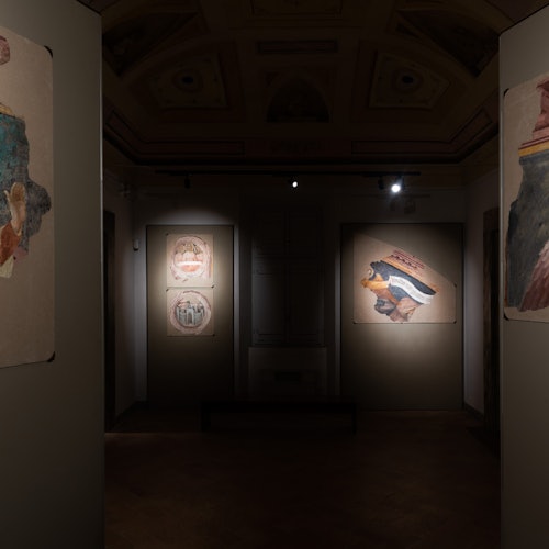 Dálítið dimmt gallerí sem sýnir forn freskúr á veggjum, með kastljósum sem varpa ljósi á tiltekna hluti á drapplita bakgrunn.