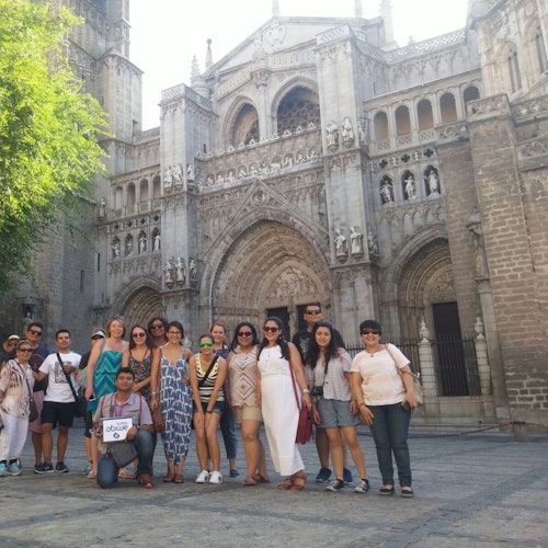 A group of people posing in front of an ornate, large stone cathedral with arched doorways and detailed sculptures.
