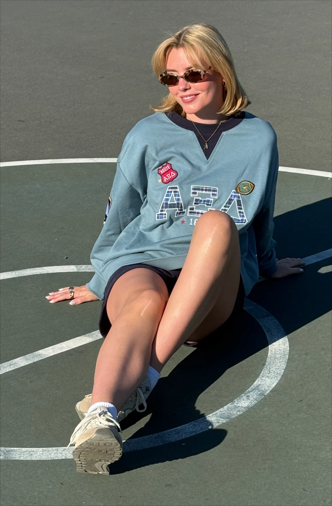 AXID's Izzy Murphy seated on an outdoor court wearing a teal retro crewneck and navy shorts.