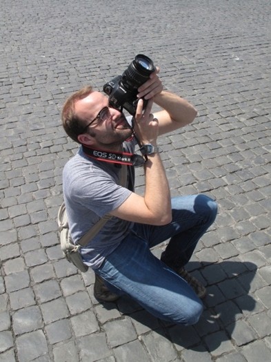 A photo of a person sitting in a stoned square and taking a picture.