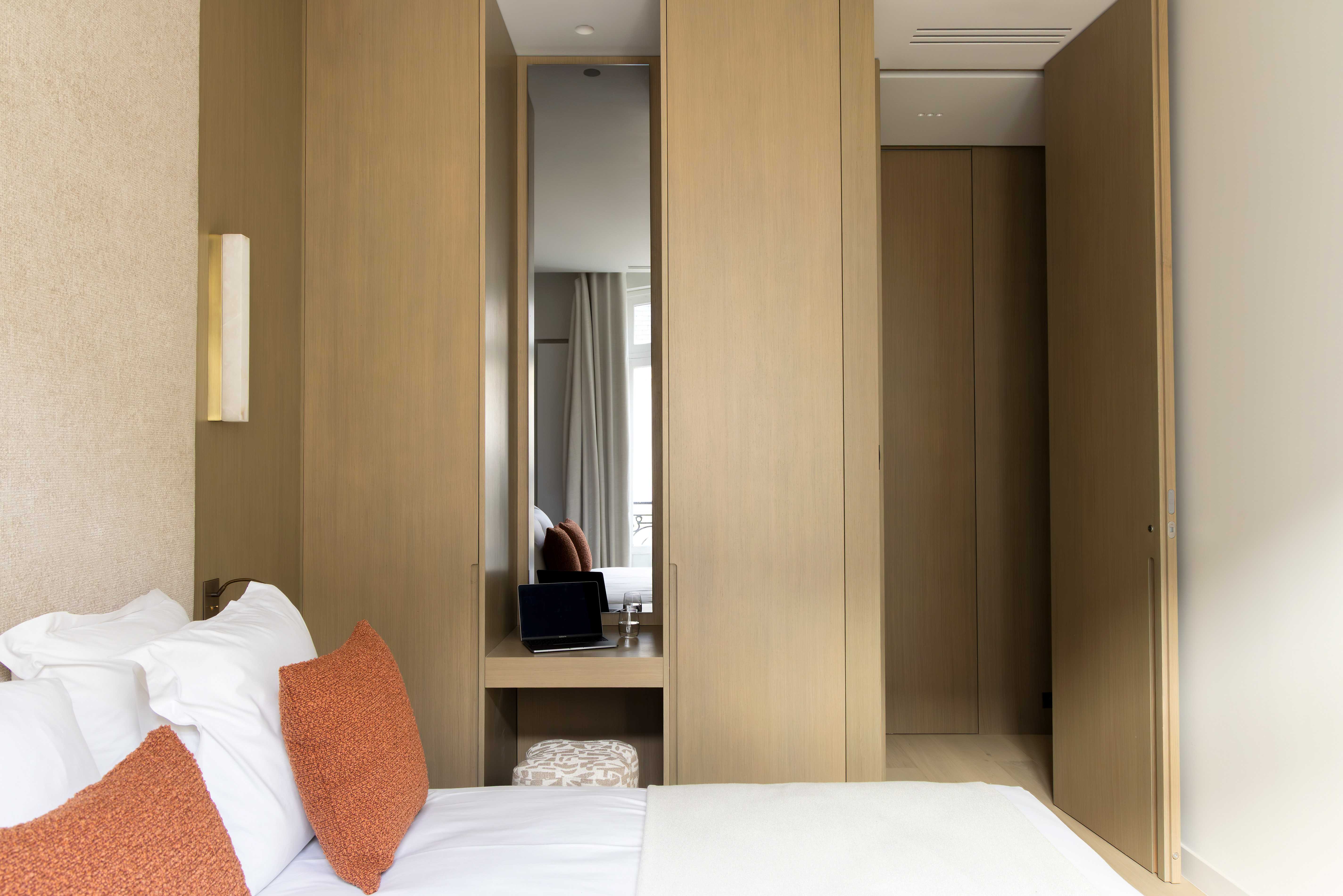 Chambre secondaire avec dressing en bois clair ouvert, miroir integre et acces vers couloir salle de bain