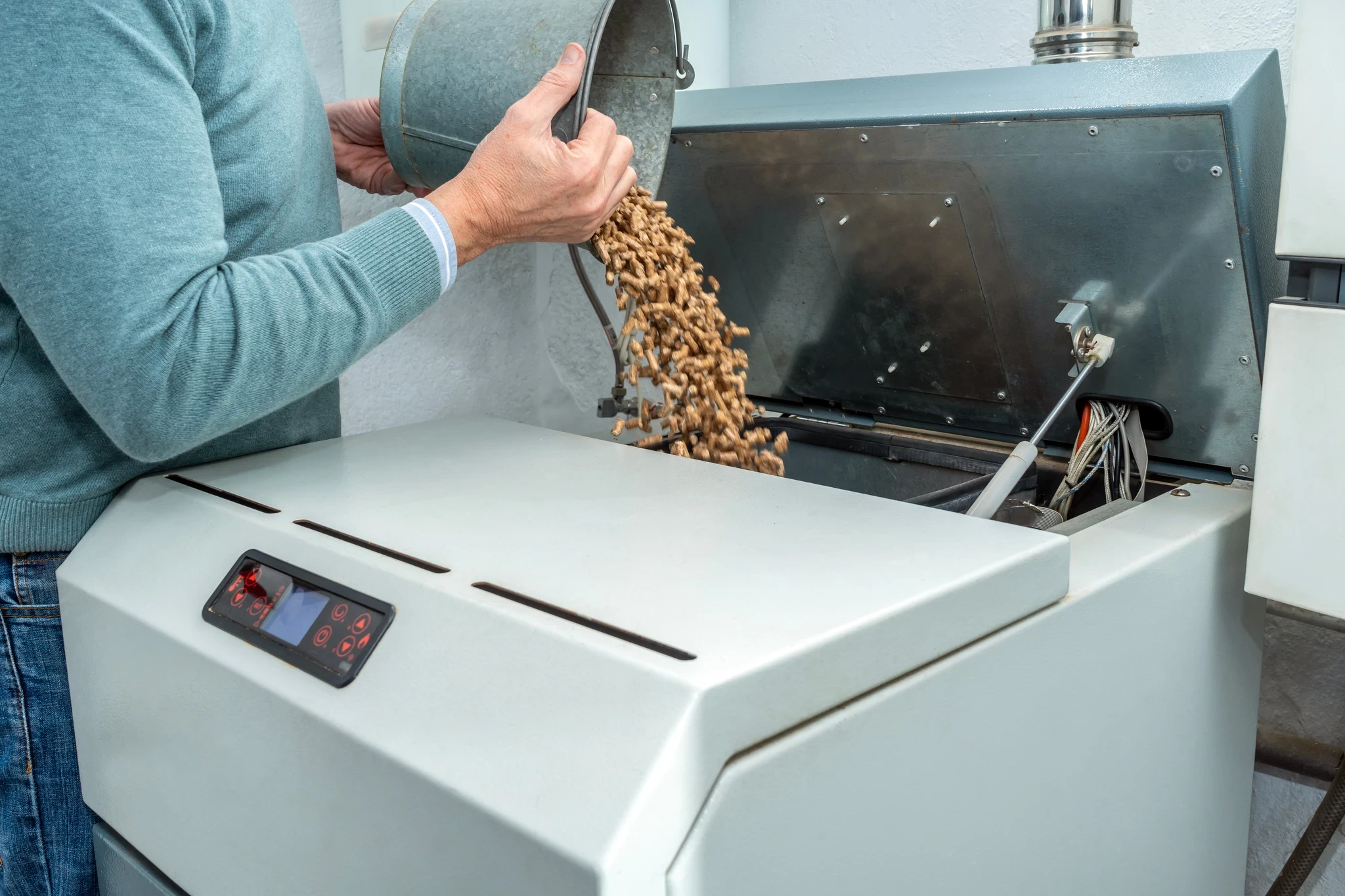 Person pouring wood biomass pellets from a bucket into the hopper of a boiler.