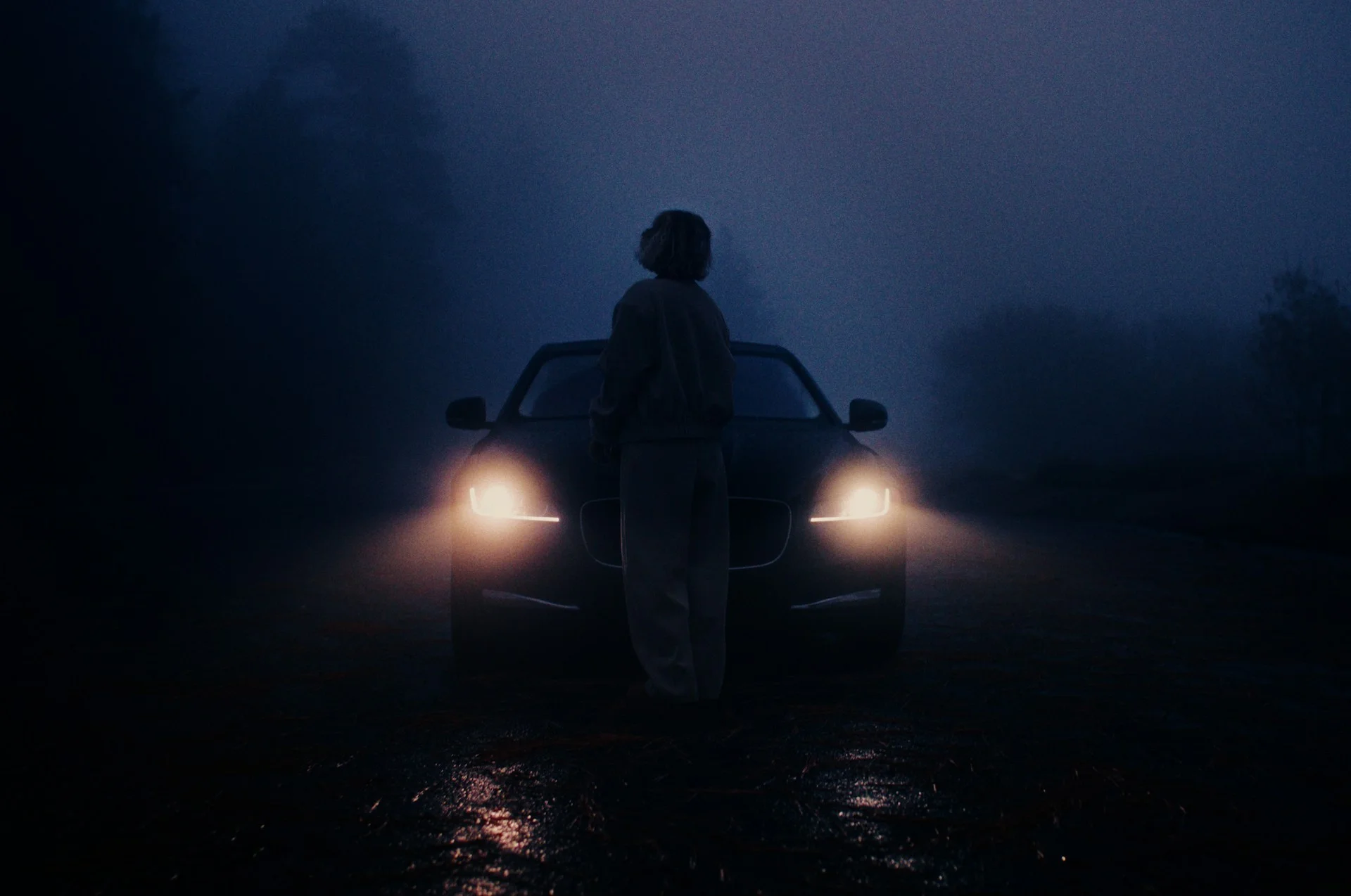 person standing in front of a car's headlights in the dark