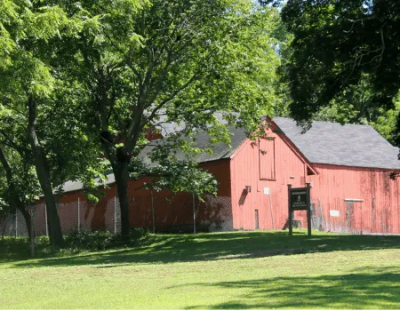 A red barn surrounded by lush green trees and grass on a sunny day.