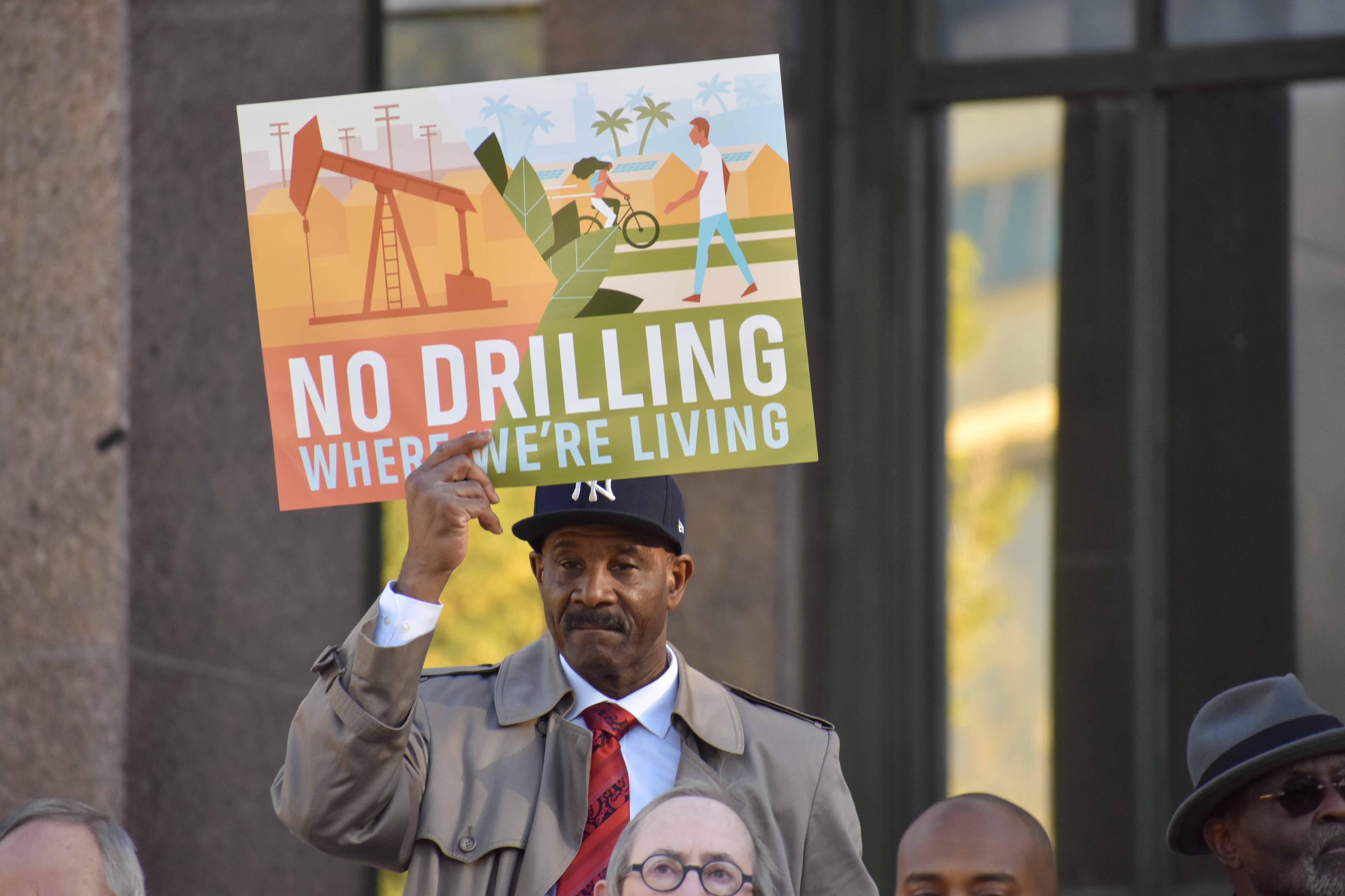 A man at a rally against Big Oil holding a sign that reads "No drilling where we're living."