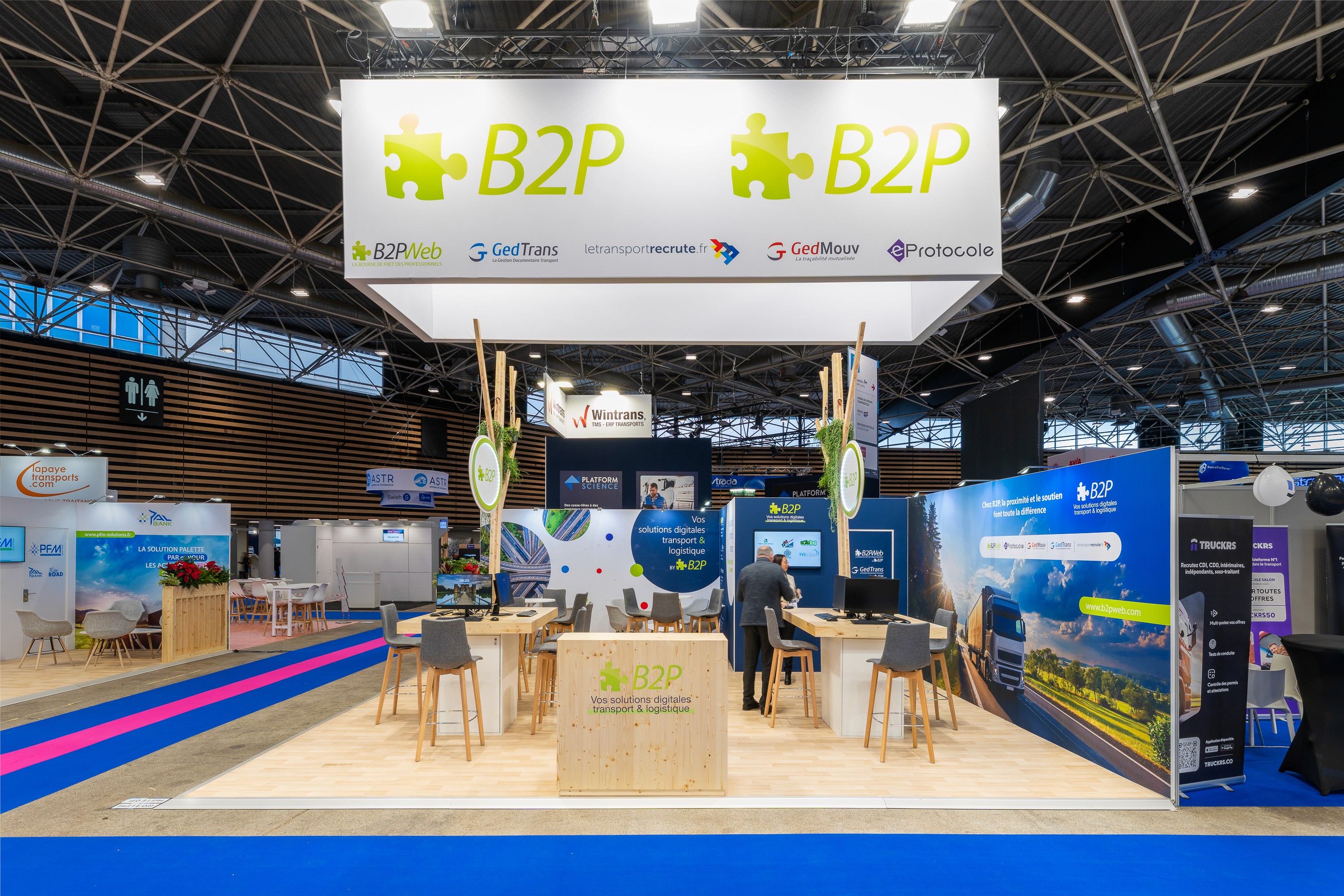 Stand B2PWeb Solutrans Lyon 2025 – aménagement stand sur-mesure bois clair et végétaux avec signalétique suspendue, réalisé par Expace