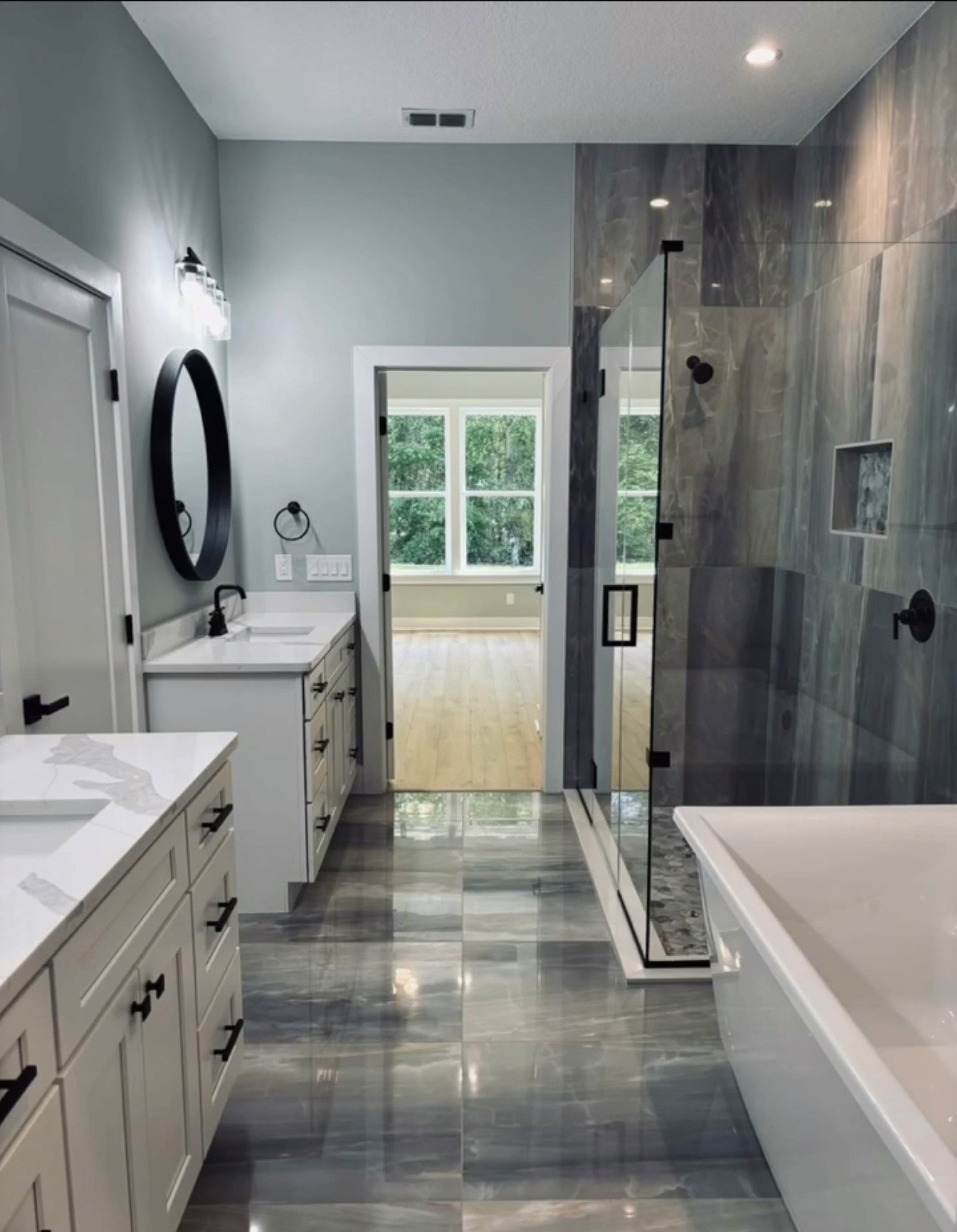 Soaking tub and glass shower detail with gray marble tile, black fixtures, and mosaic floor tile