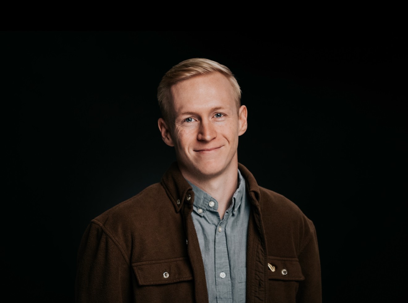 Man with curly hair wearing brown hat and dark shirt.
