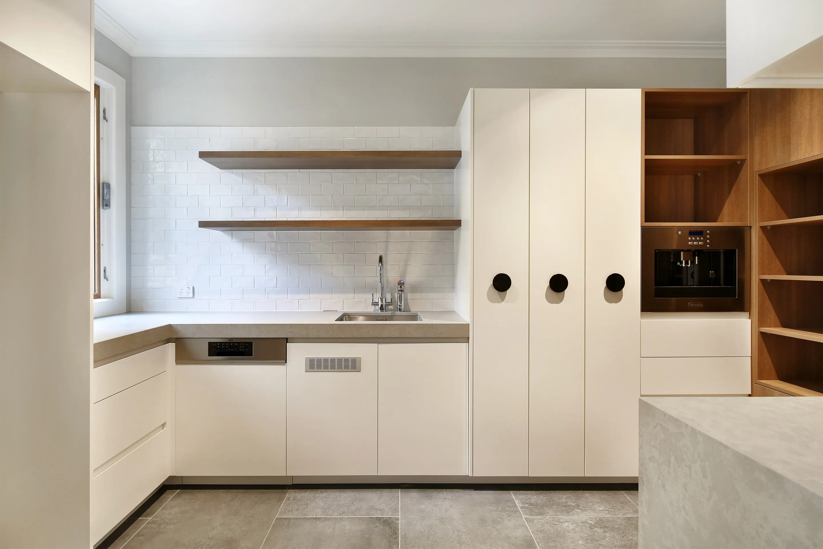 Butler's pantry with cream cabinetry, timber open shelves over a white subway-tile splashback, stone benchtop, undermount sink, built-in coffee machine and warm timber shelving