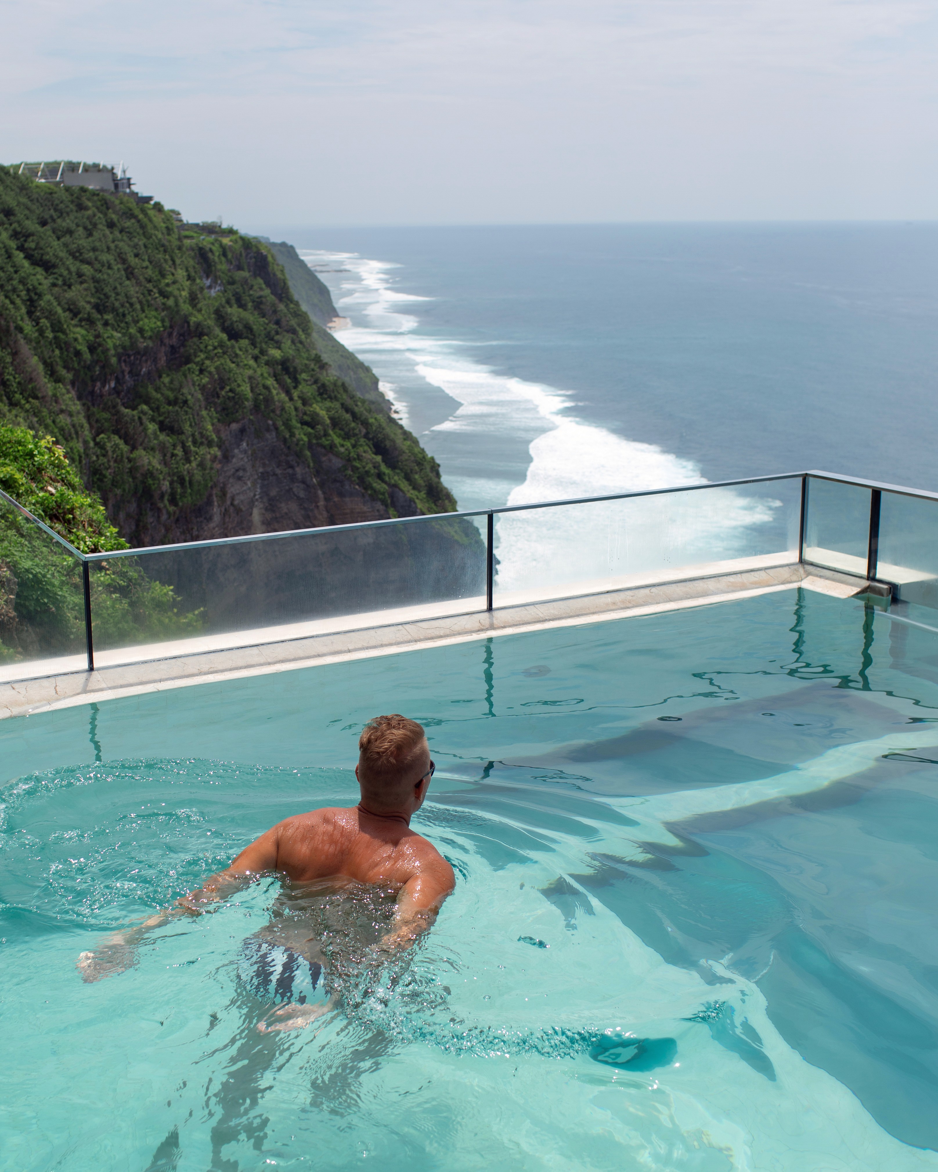 A person swims in an infinity pool overlooking a dramatic cliffside view and vast ocean, creating a serene and expansive atmosphere.