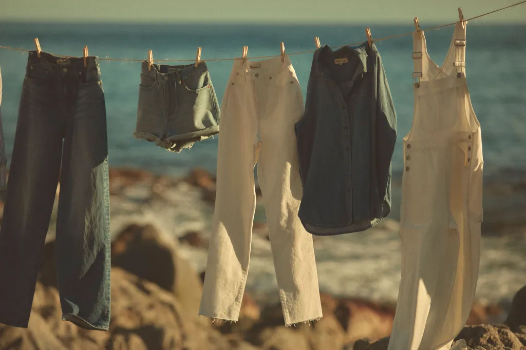Clothes hanging on a line near a beach, with the ocean and a clear sky in the background.