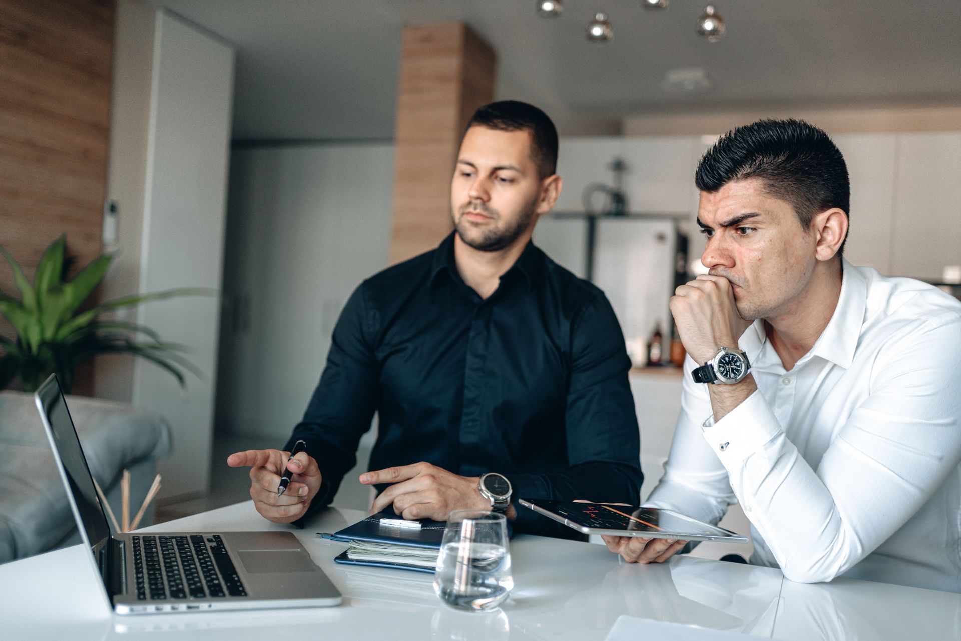 Two businessmen reviewing figures on a laptop and tablet at a desk