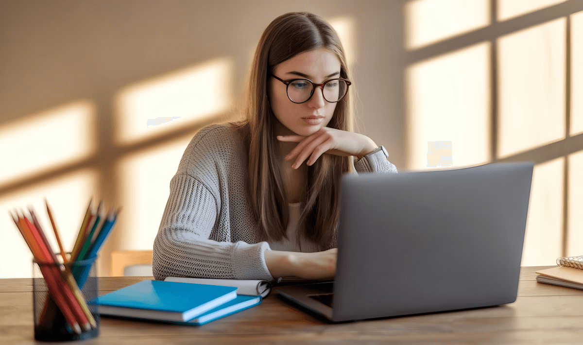 Woman with glasses working focused on laptop at wooden desk