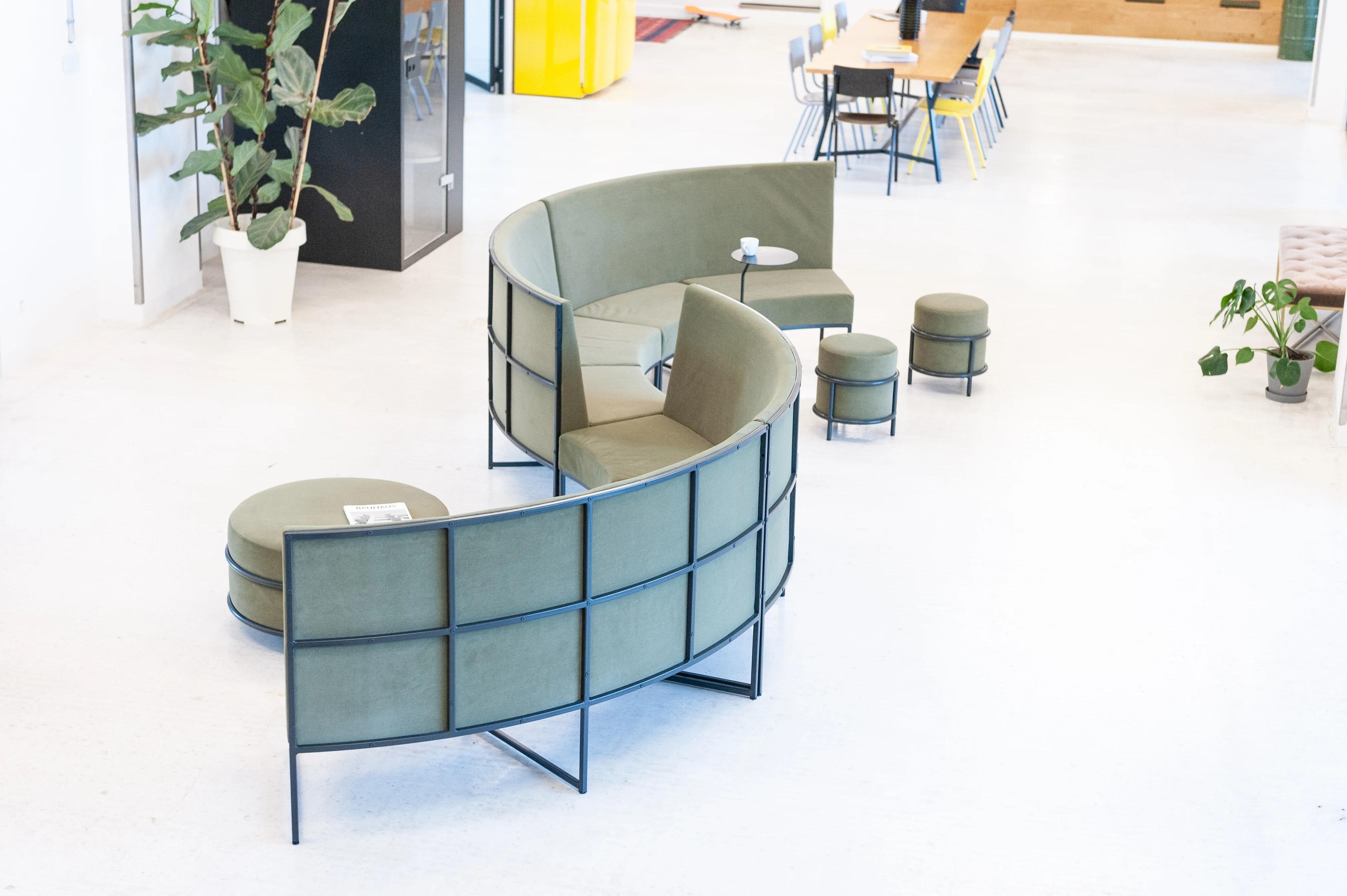 Bird's-eye view of the snake-shaped green lounge sofa at LA RED with poufs, a side table and potted plants on a light concrete floor, dining tables visible at the top.