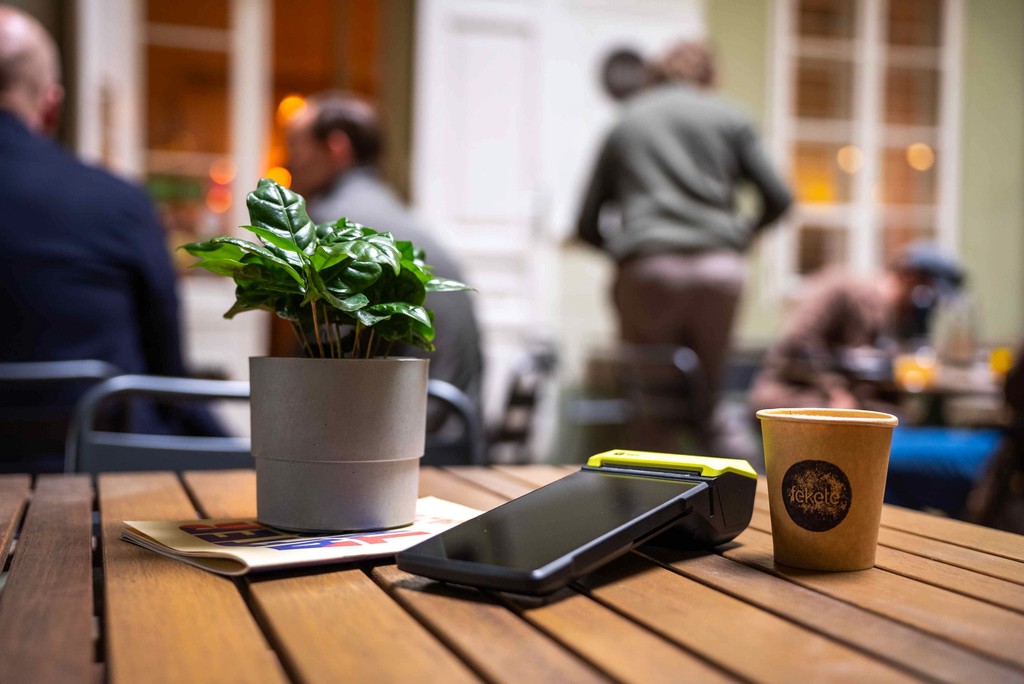 a Teya card machine on a restaurant table, with a cup of coffee and a plant next to it.
