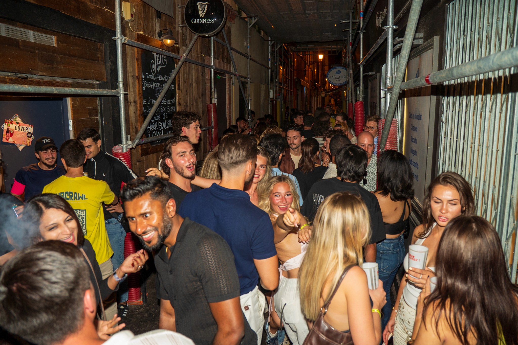 Crowded street scene with international travelers socializing between bars during a bar crawl in Nice showing the lively nightlife atmosphere and first time pub crawl experience in the French Riviera
