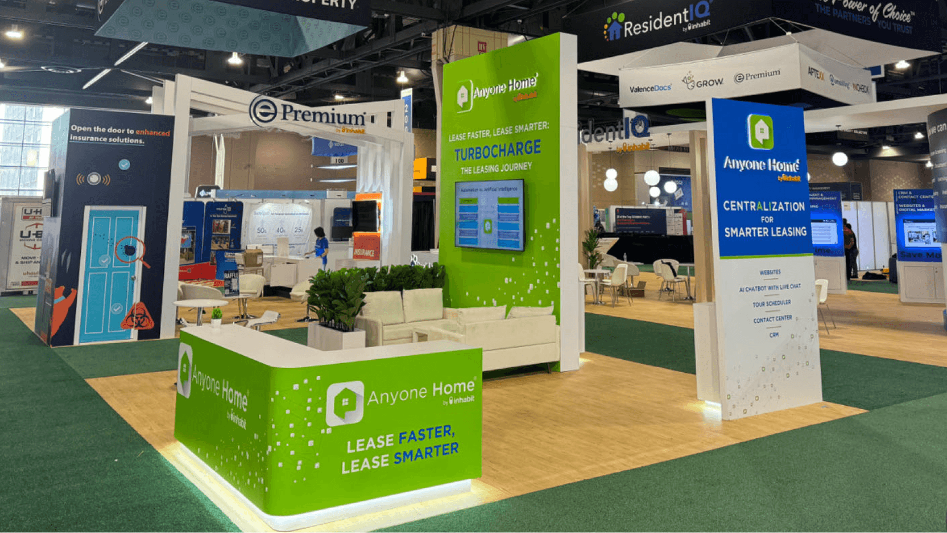 Anyone Home NAA 2024 20x20 professional service booth with green branded reception counter, tall leasing solution display tower, lounge seating, and open visitor flow.