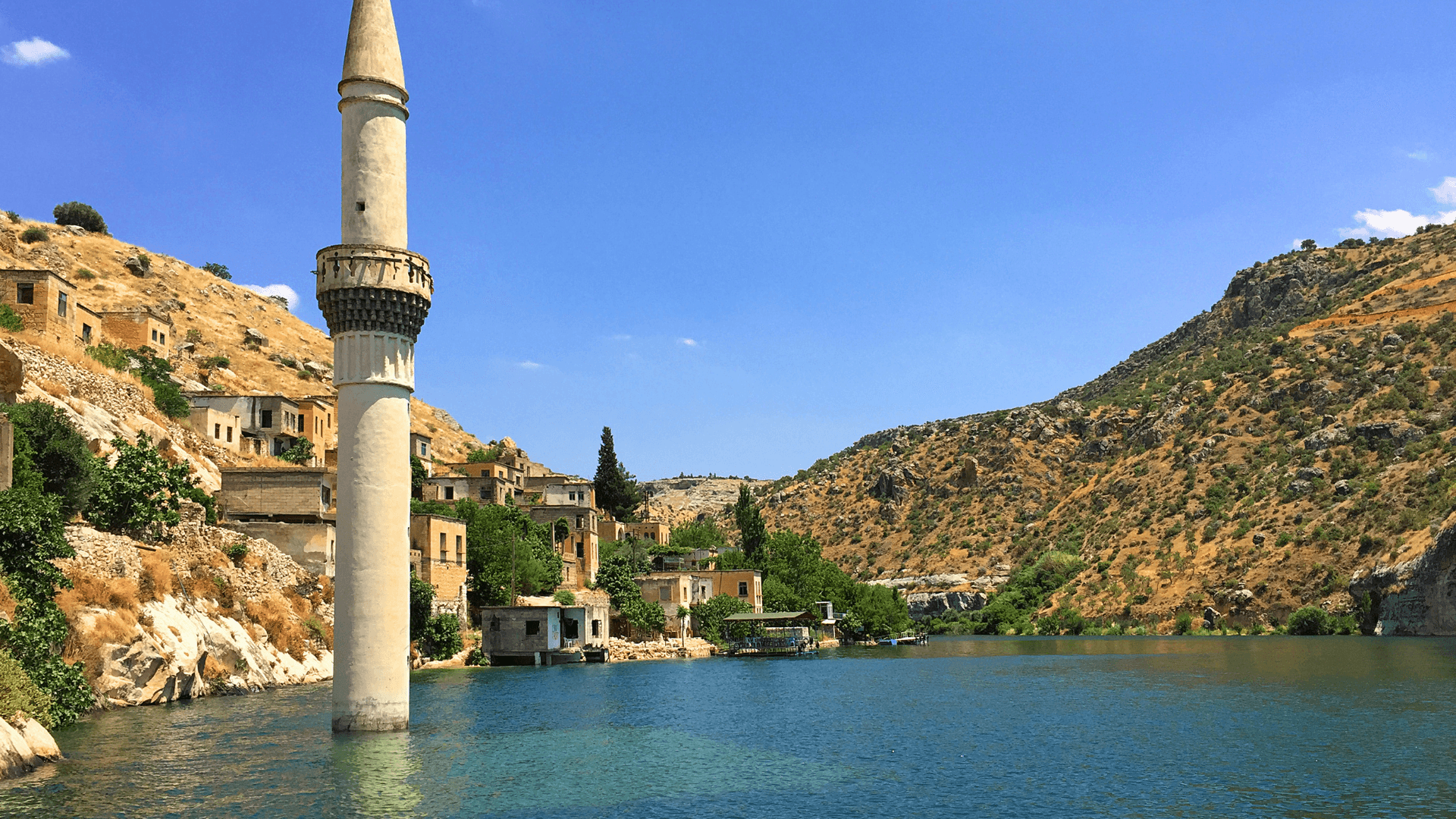 The partially submerged mosque minaret of Halfeti, a Cittaslow “Slow City” in Southeastern Türkiye, surrounded by turquoise waters and hillside houses.
