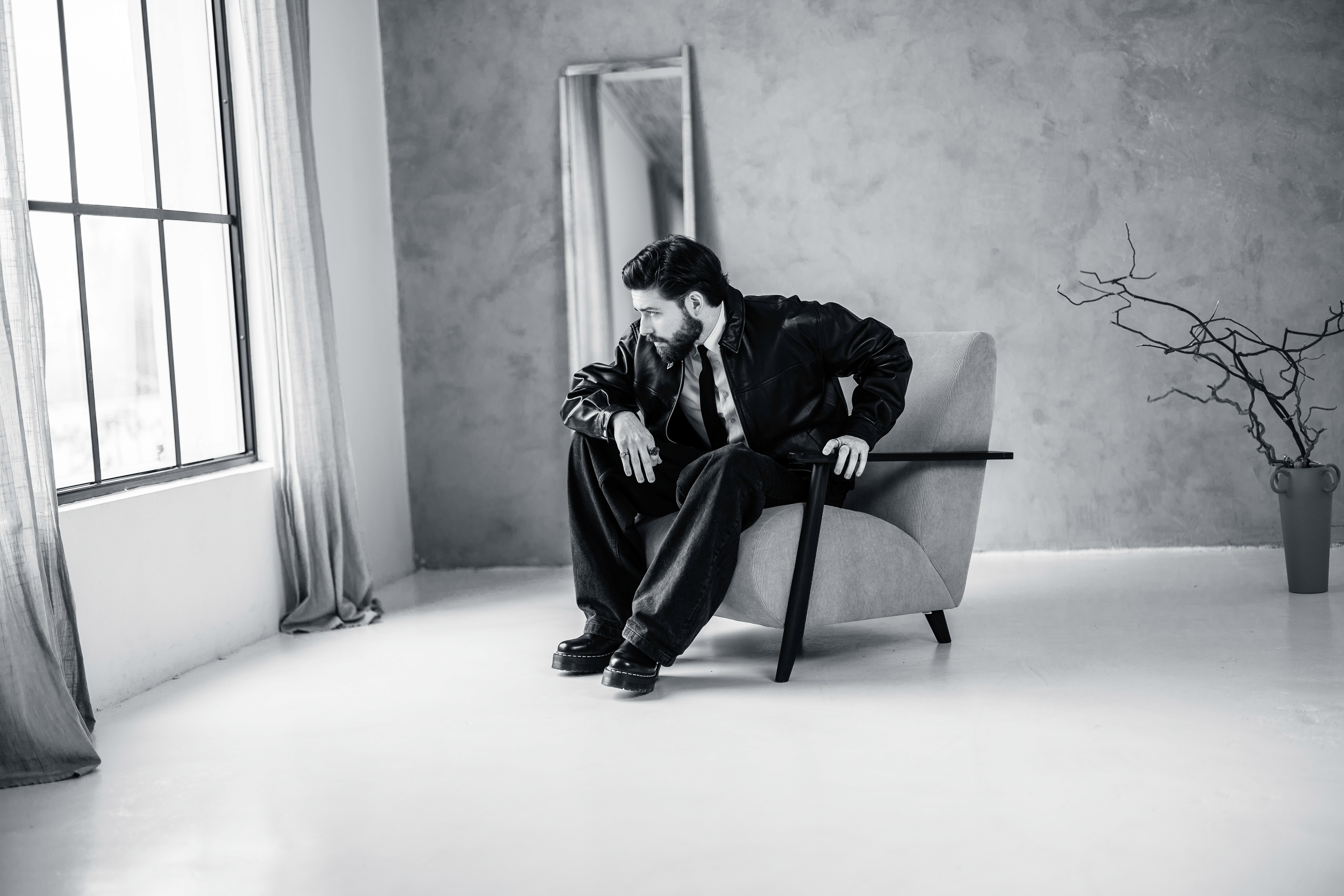Férfi modern fotóstúdióban, bőrfotelben ül, laza pózban, fekete-fehér hangulatban.