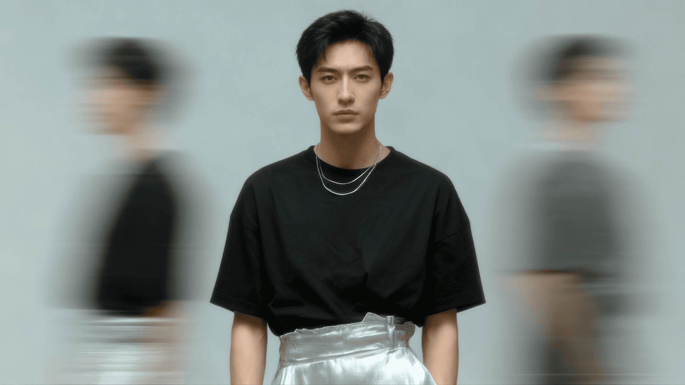 A stylish individual in a black shirt and silver pants stands against a blurred background, creating a dynamic and modern aesthetic.