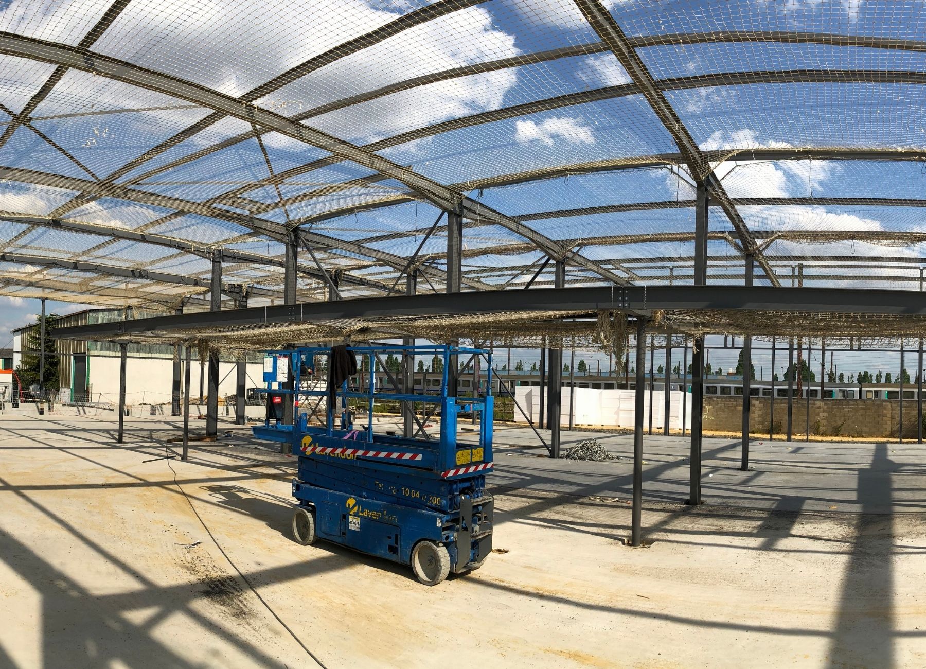 Structure métallique d’un bâtiment en cours de montage avec nacelle élévatrice sur dalle béton.